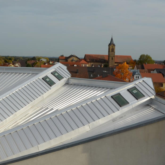 Ein Kalzip Aluminium Dach in fertig gedecktem Zustand. Im Hintergrund ist ein Stadtpanorama mit Kirche zu sehen